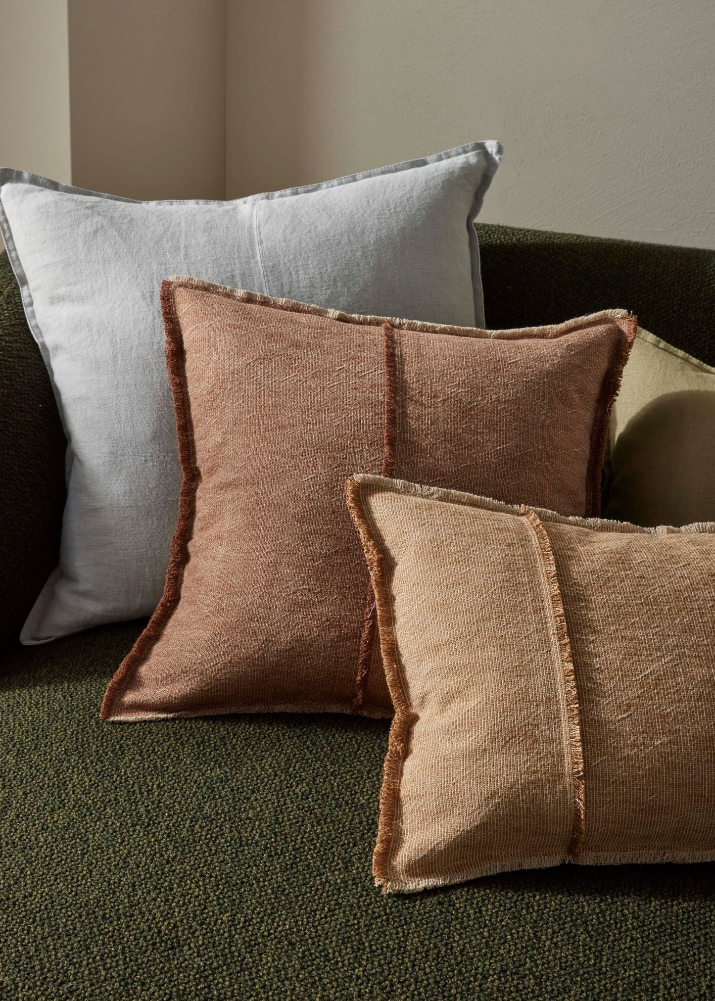 Three textured pillows in brown and gray on a green sofa.