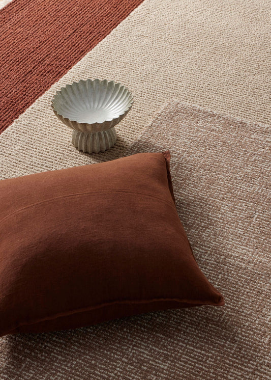 Brown pillow on a textured carpet with a decorative bowl.