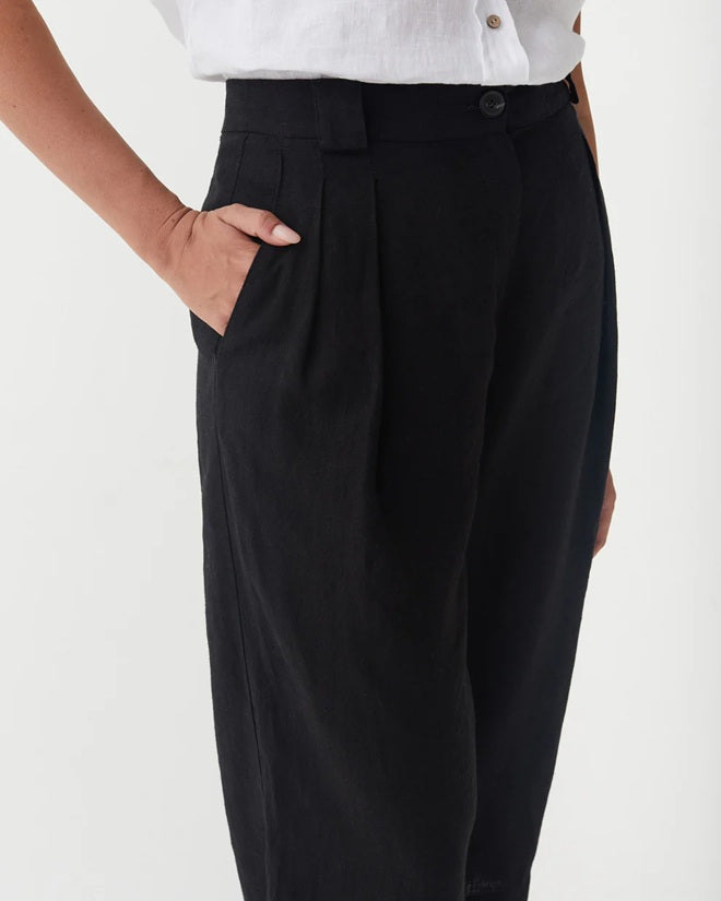 Black pleated pants worn with a white shirt on a plain background