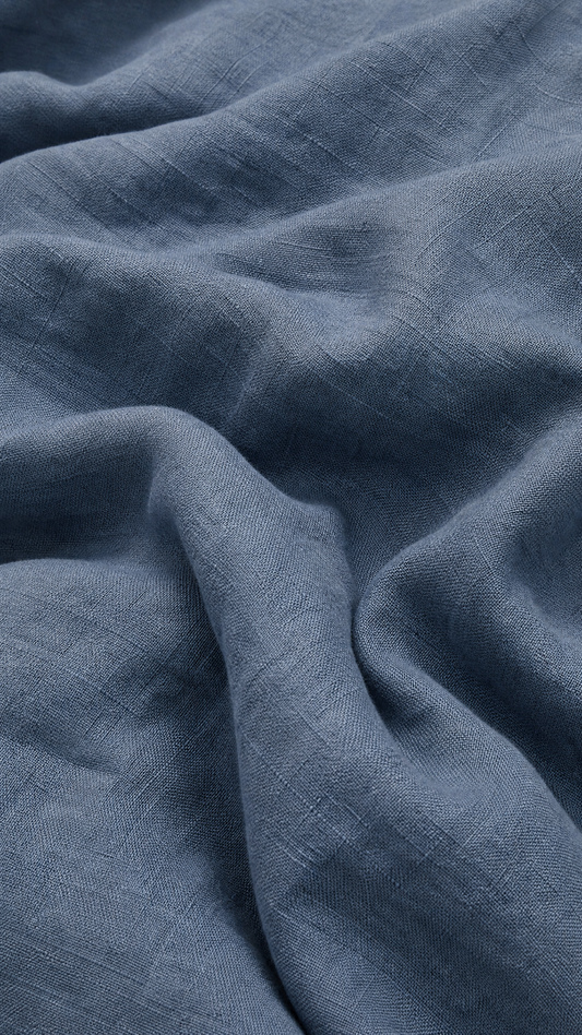 A close-up of draped slate blue linen fabric with a visible woven texture and soft folds.