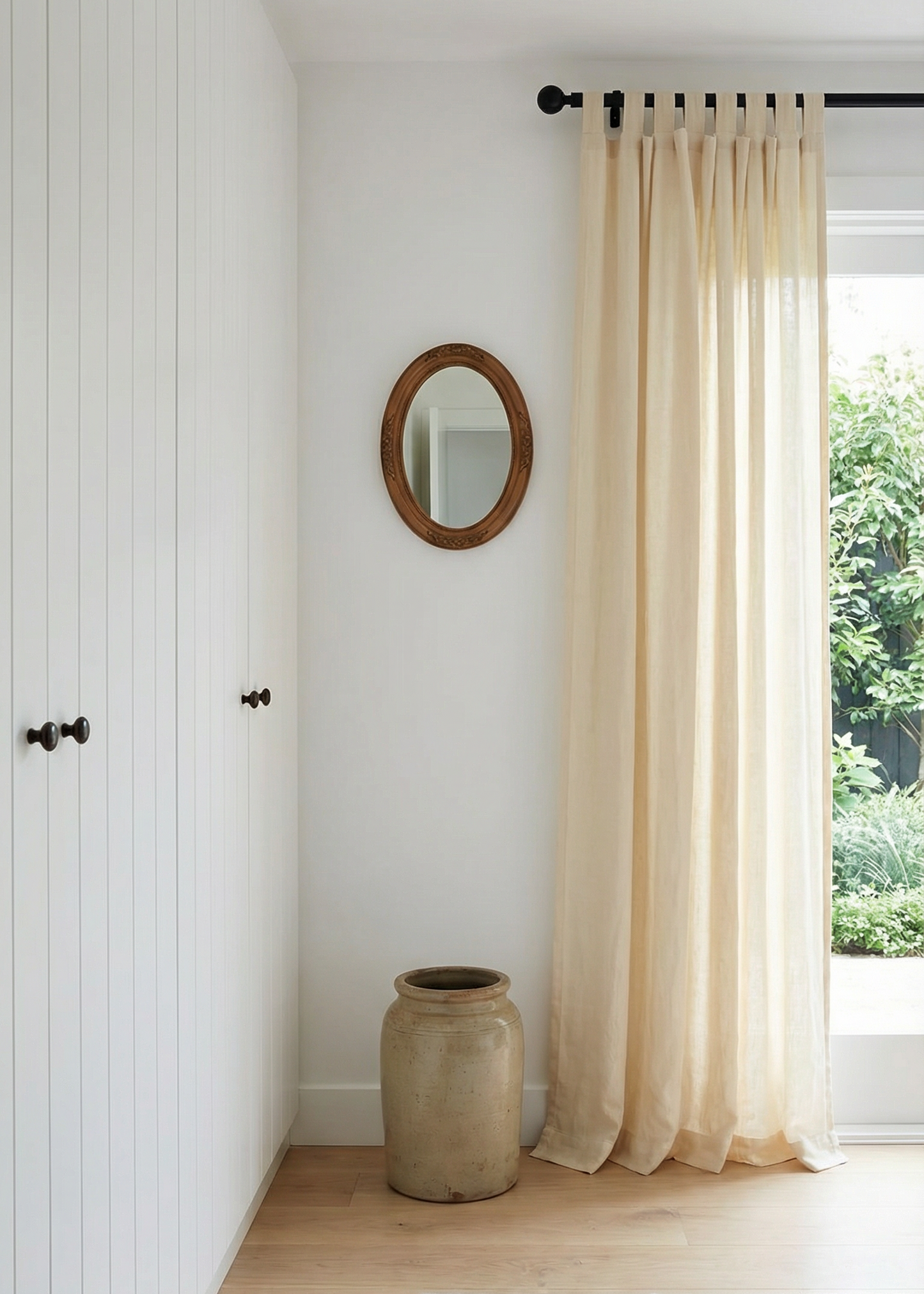 Nest living room with white walls, a large window with beige curtains, a round mirror, and a textured rug.