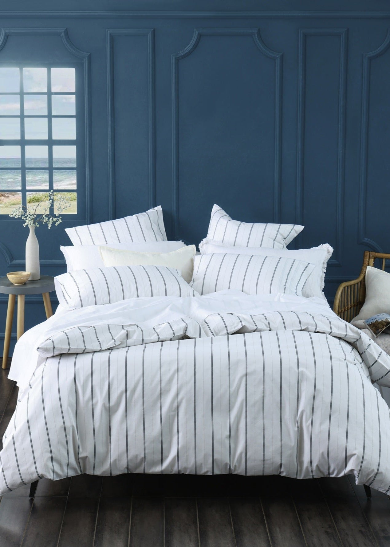 Striped bedding set on a bed in a room with blue paneled walls and a window.