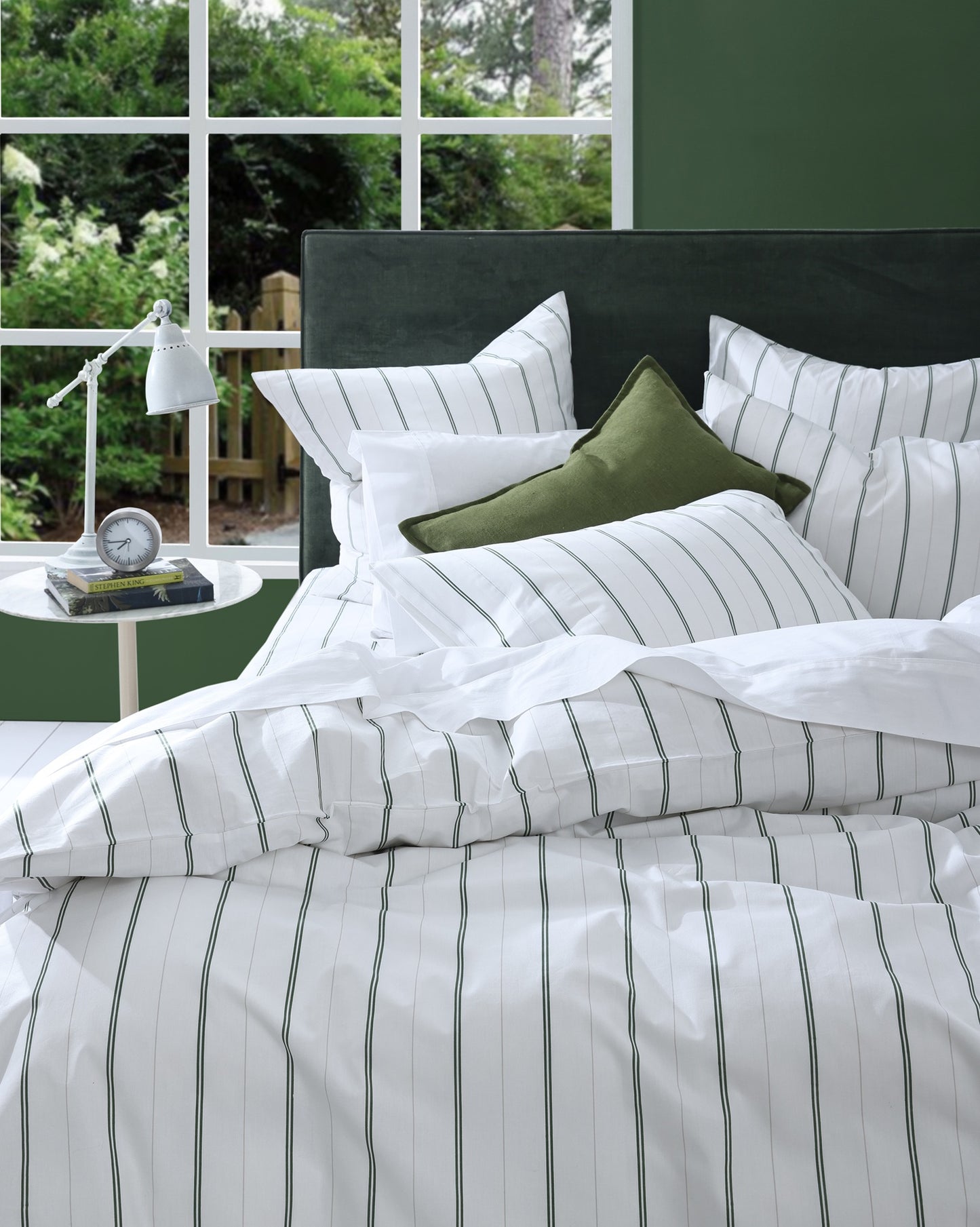 Striped bedding set on a bed with a green pillow and window view.