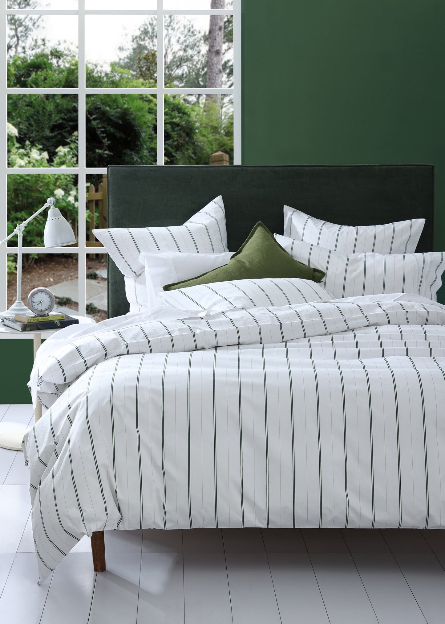 Bed with striped bedding and green pillows in a room with large windows.