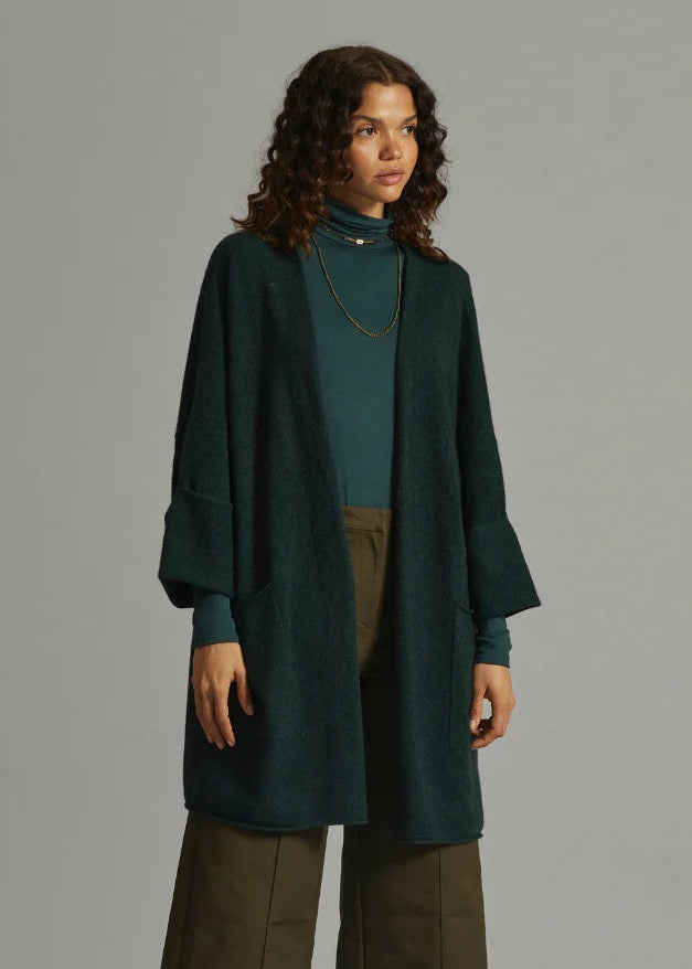 Woman wearing a green coat and brown pants against a gray background