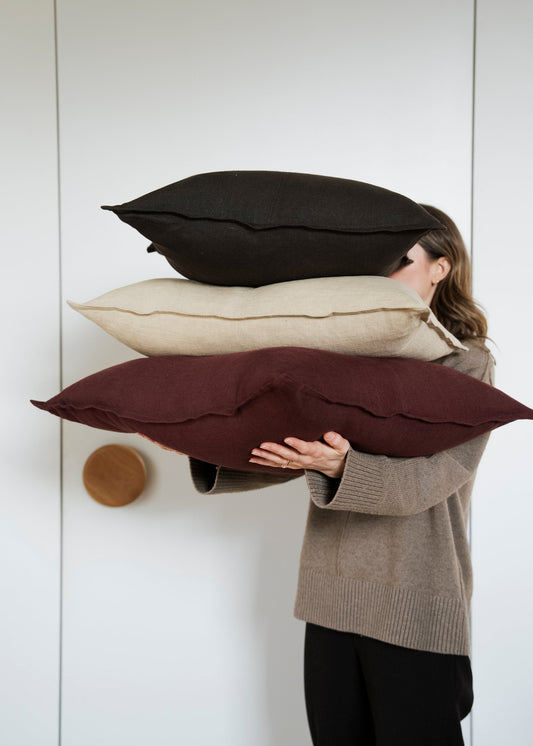 Person holding three pillows of different colors against a white wall