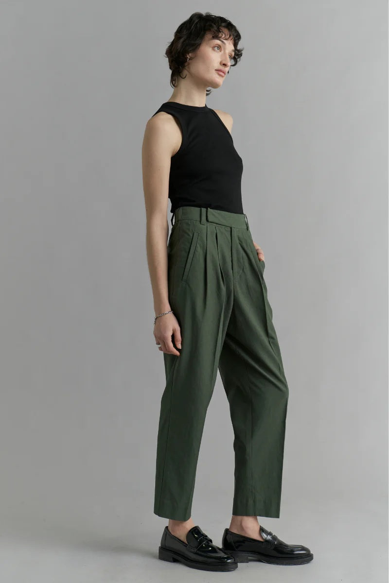 Woman wearing a black sleeveless top and green pleated pants on a gray background