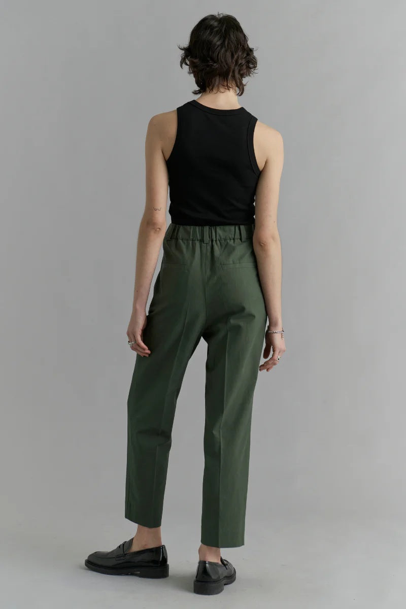 Person wearing a black sleeveless top and green pants on a gray background