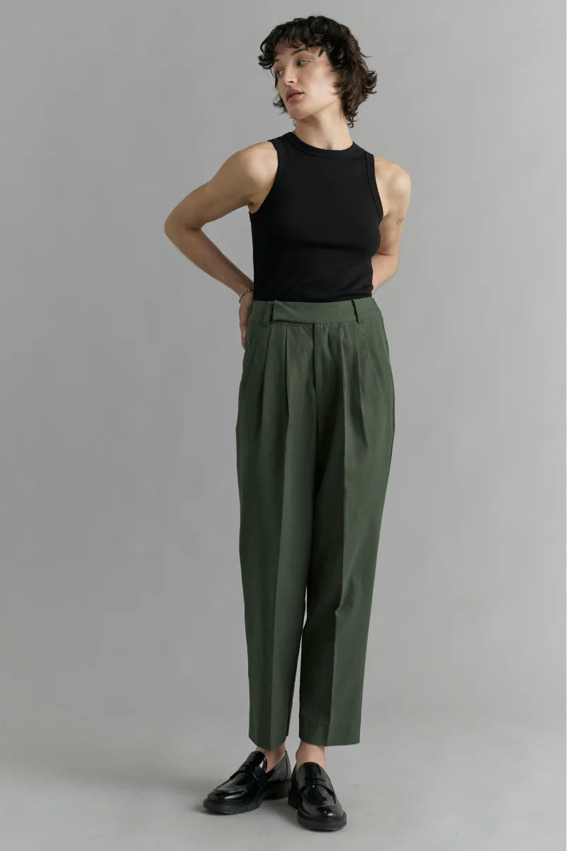 Person wearing a black sleeveless top and green high-waisted pants on a gray background