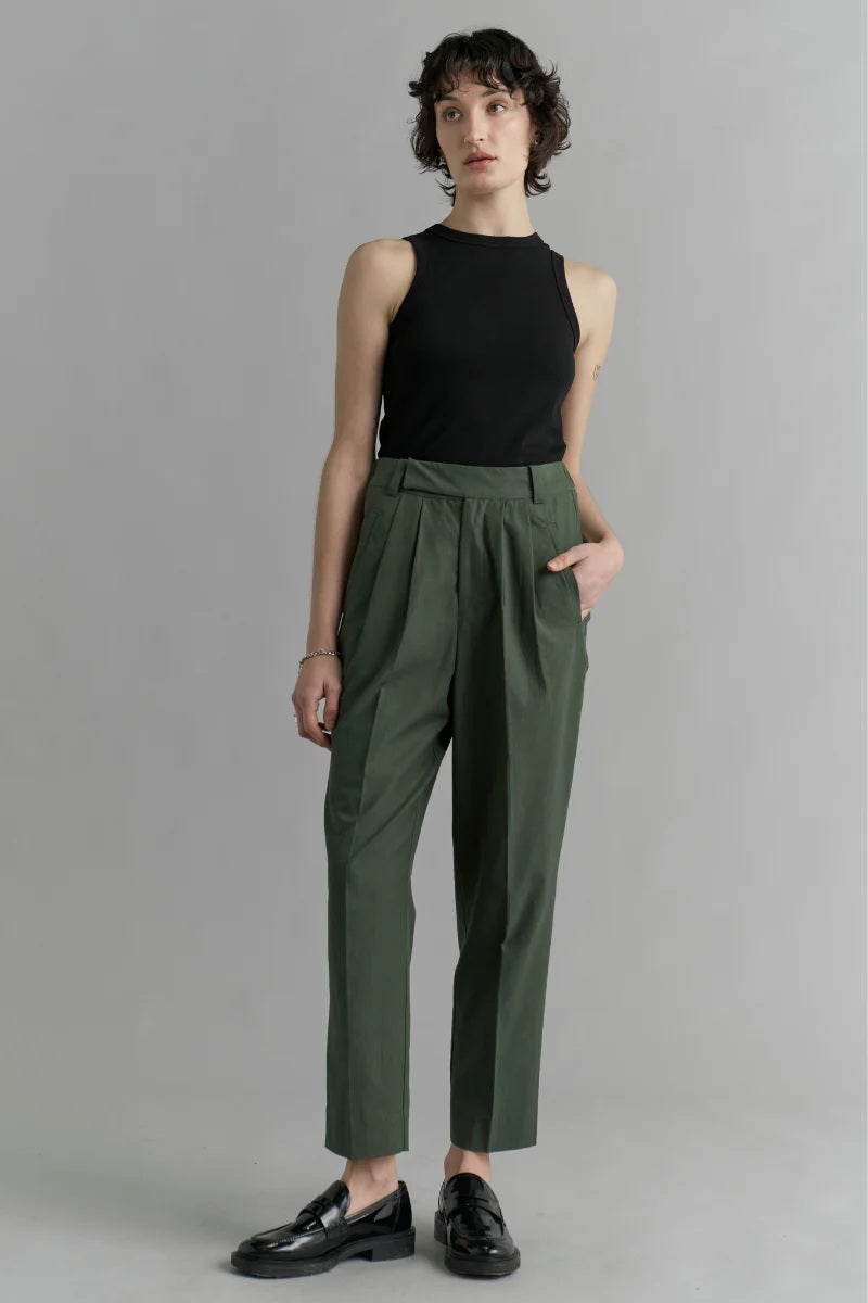 Woman wearing a black sleeveless top and green pleated pants against a gray background