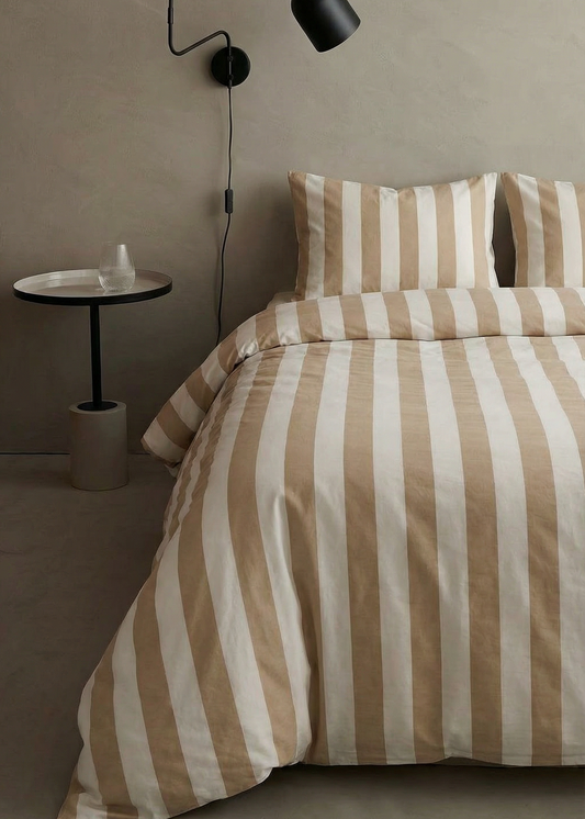 Bed with striped bedding in a room with a wall lamp and small table.