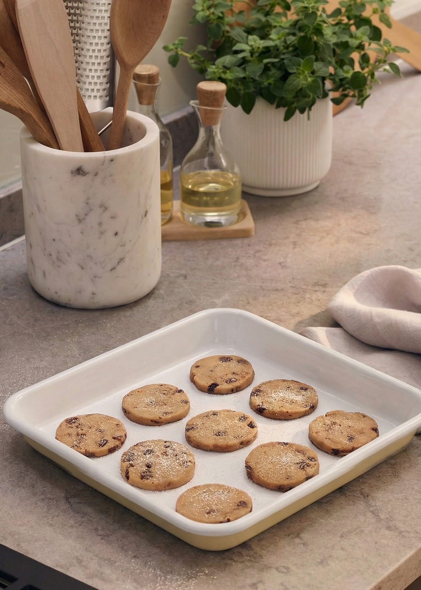 Cookies on a baking tray with kitchen utensils and plants in the background