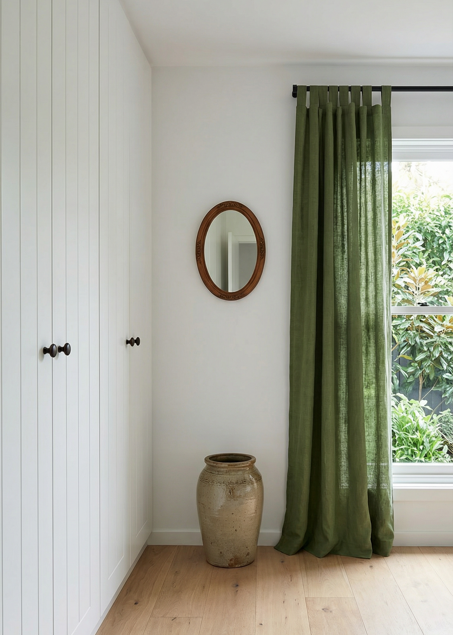 Room interior with green curtain, round mirror, and vase on a wooden floor.