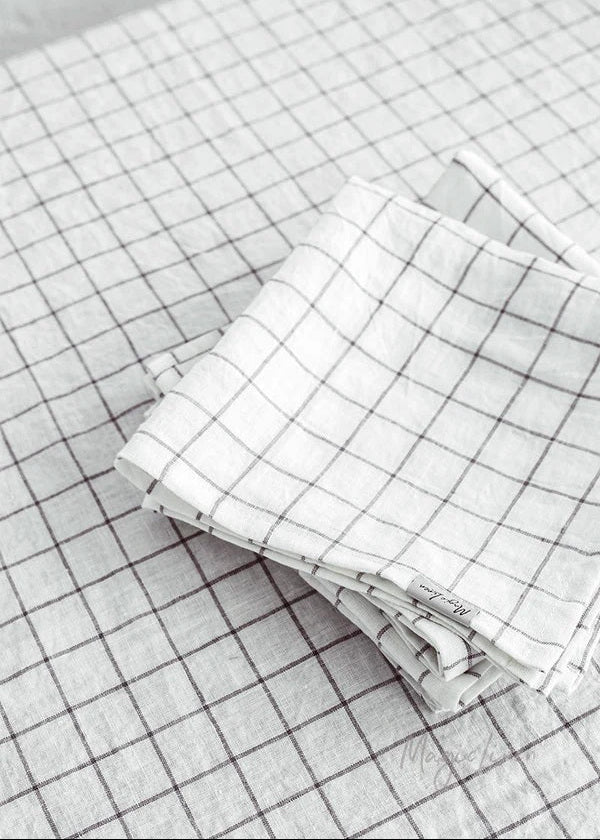 A pair of folded linen napkins with a charcoal grid pattern, placed on a similar patterned surface.