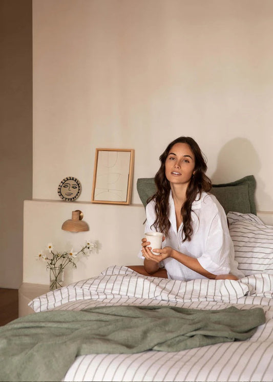 Woman sitting on a bed holding a mug in a cozy bedroom setting.