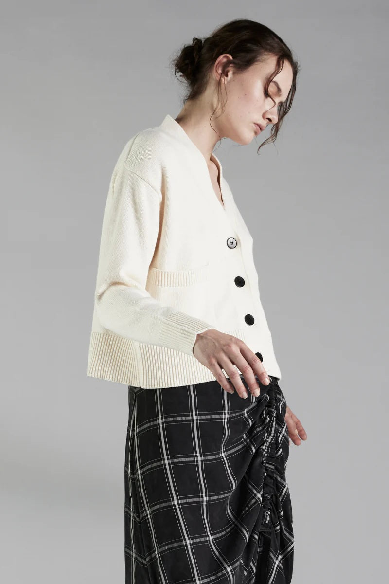 Woman wearing a cream-colored cardigan with black buttons on a gray background