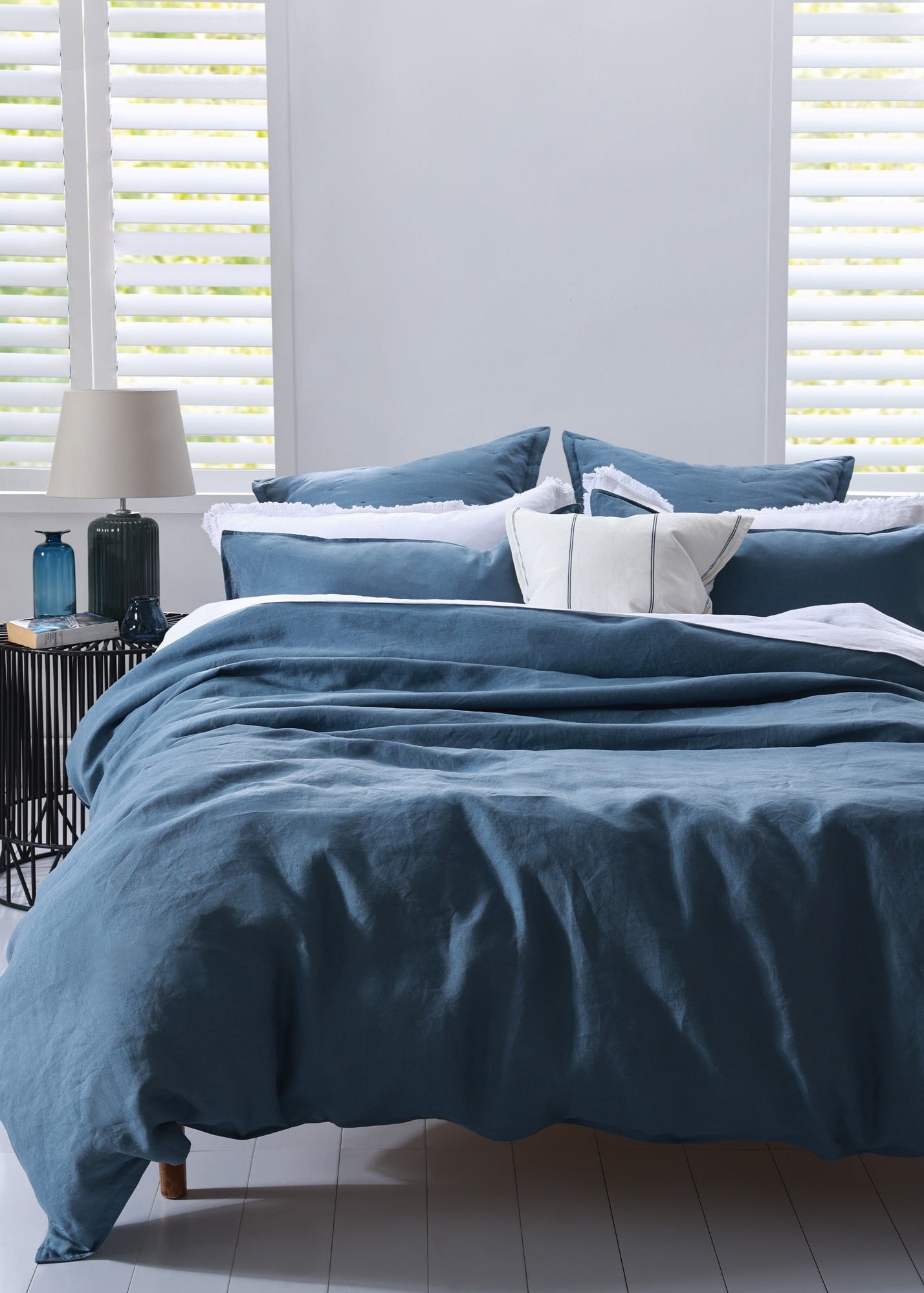 Blue bedding set on a bed with white pillows in a room with light gray walls and white blinds.