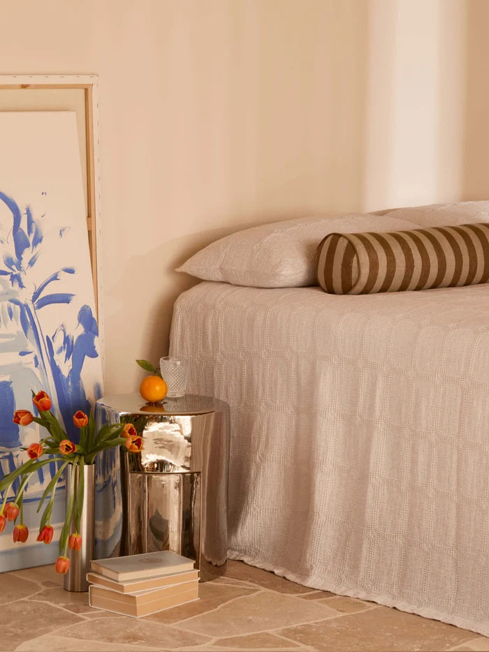 Neatly made bed with striped pillow, side table with flowers and books, and abstract art on wall.