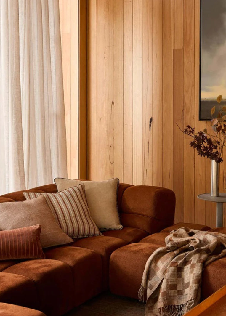 Cozy living room with brown sectional sofa, wooden walls, and a painting.
