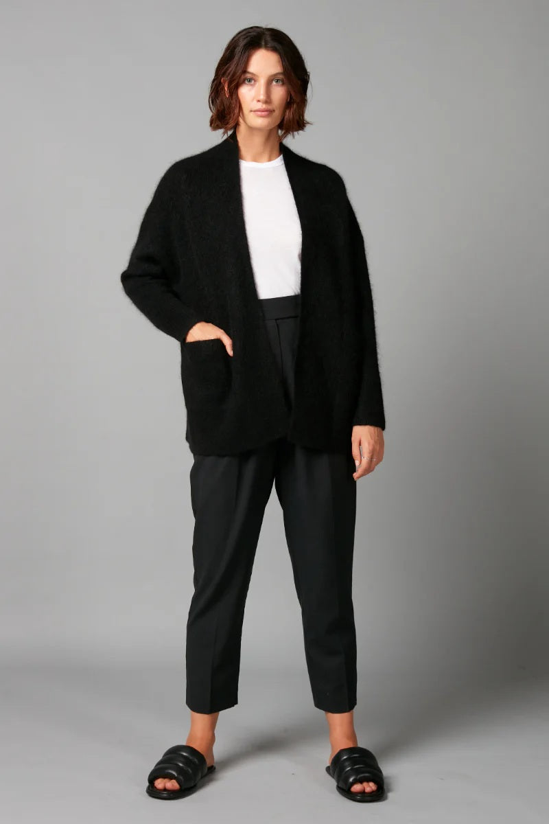 Person wearing a black coat, white shirt, and black pants on a gray background