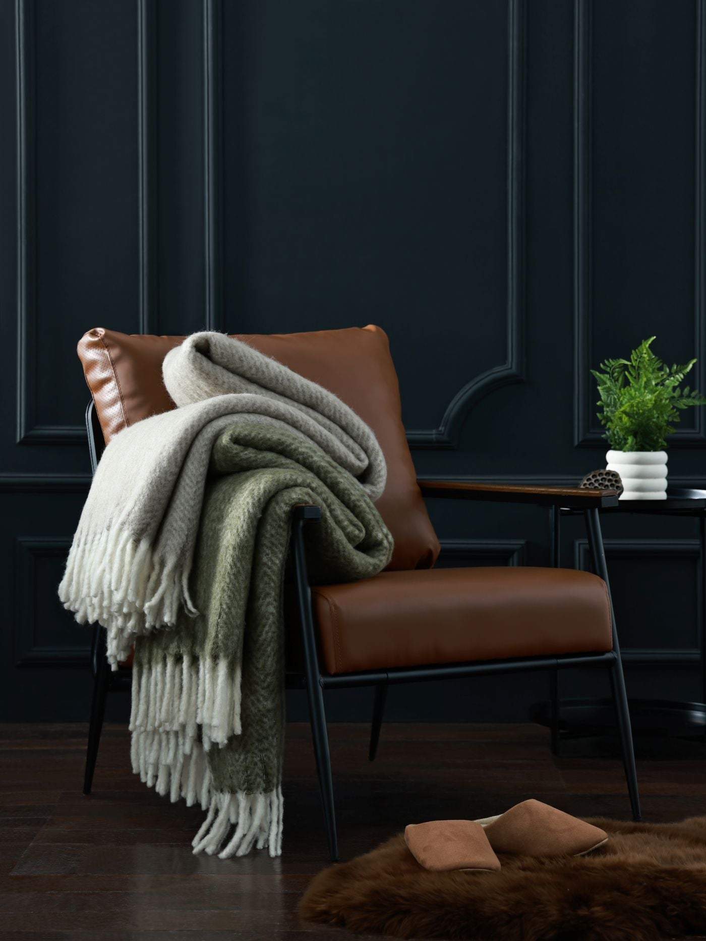 Brown leather chair with a green and white blanket draped over it against a dark paneled wall.