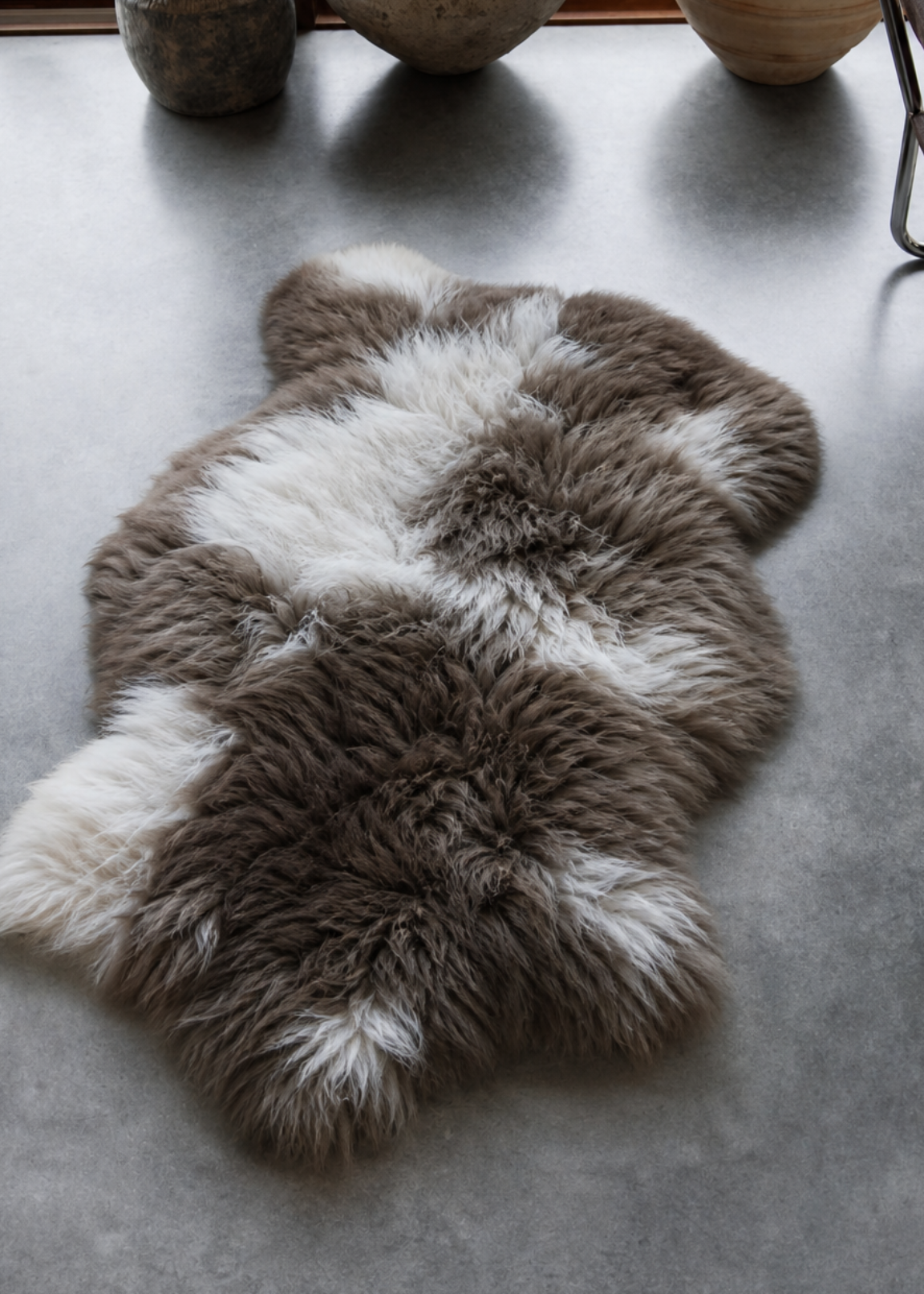 Sheepskin rug on a concrete floor with decorative vases and a chair in the background.