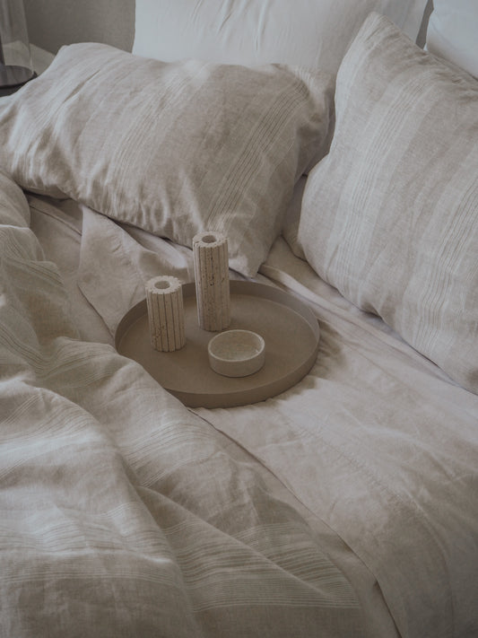 Decorative tray with cylindrical objects on a bed with white bedding