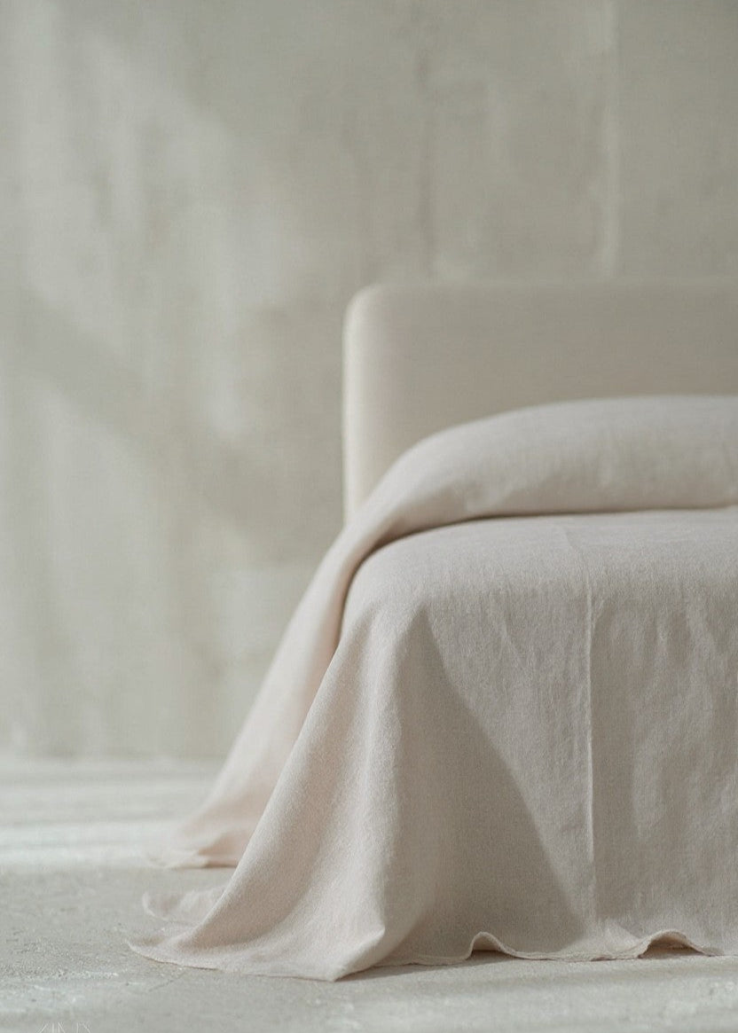 Beige blanket draped over a chair against a neutral background