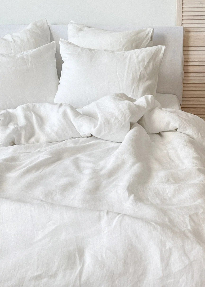 Neatly made bed with white bedding in a room with wooden flooring and a woven rug.