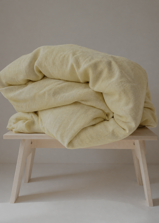 Light yellow blanket on a wooden stool against a neutral background