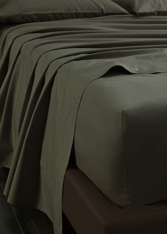 A close-up of olive green bed sheets and a matching fitted sheet on a bed, with the sheet draped over the side to show its drape and texture.