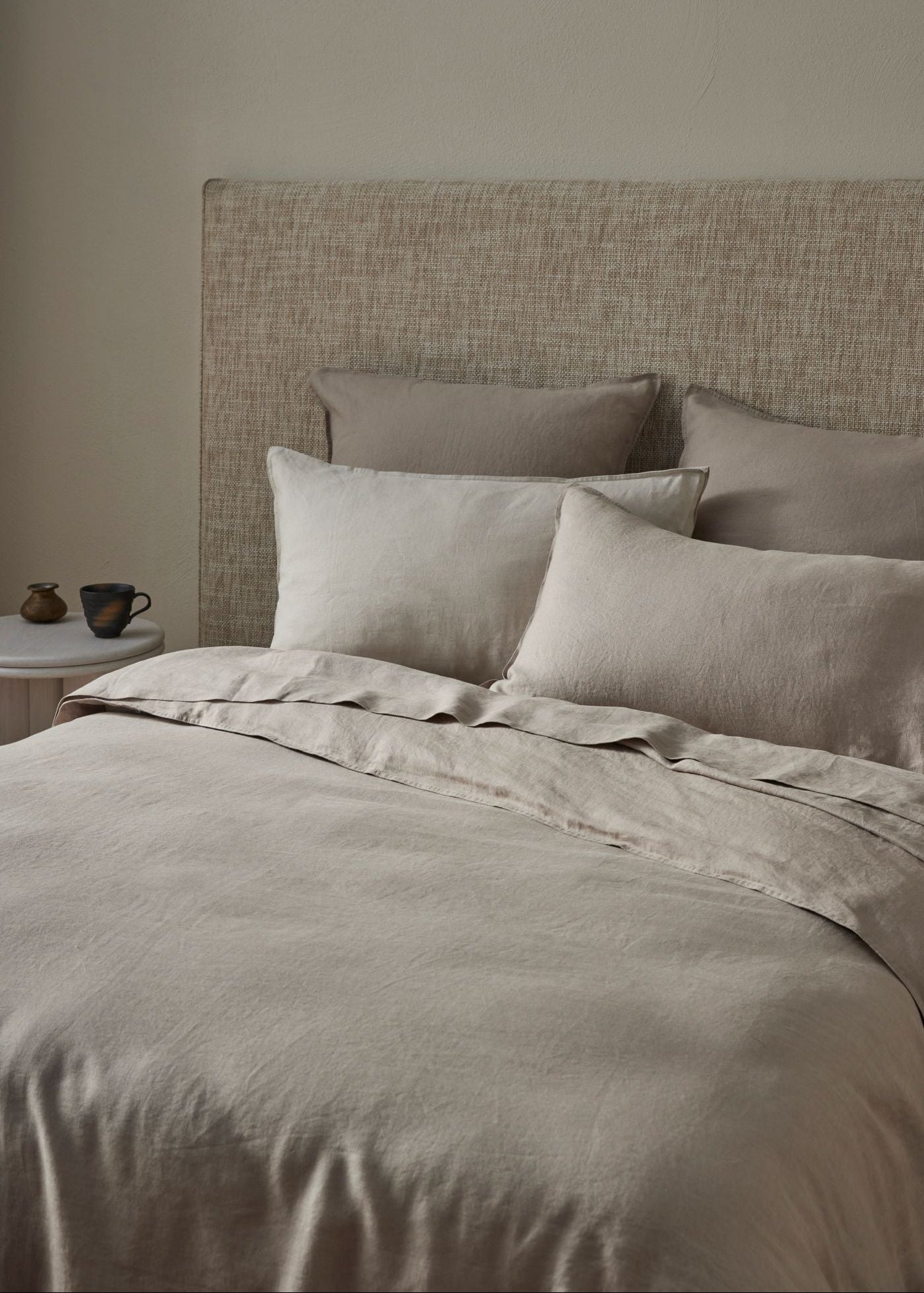 Neatly made bed with beige bedding and pillows against a neutral wall.