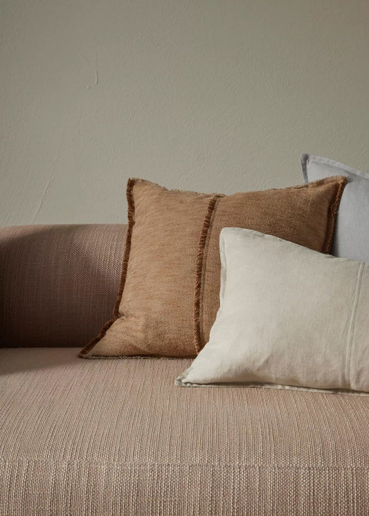Three pillows on a beige sofa against a plain wall