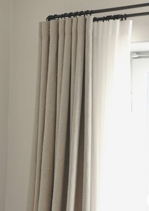 Close-up of beige textured curtains hanging on a window with a blackout panel on the top.