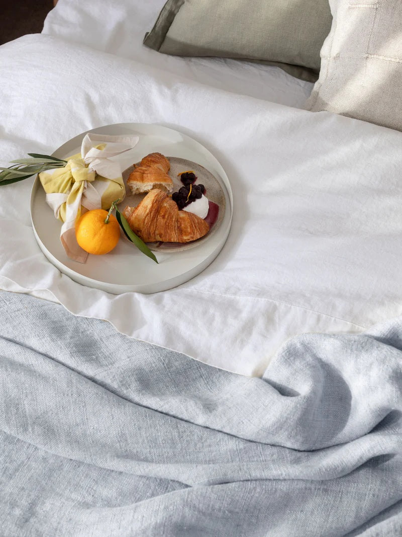 Plate with croissant, orange, and flowers on a white bedspread