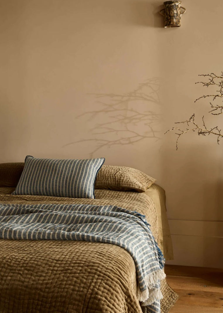 Nestled corner of a room with a bed, decorative pillow, and wall sconce.