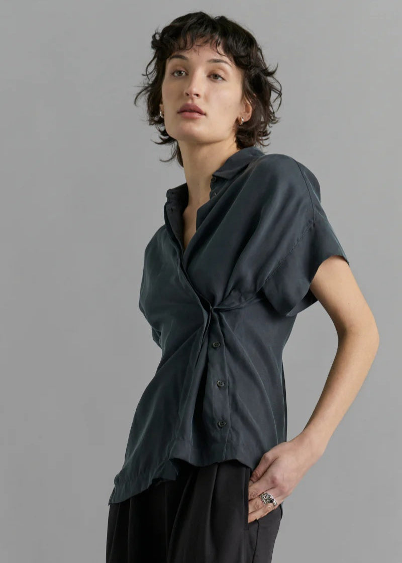 Person wearing a dark gray shirt with a knot detail on a gray background