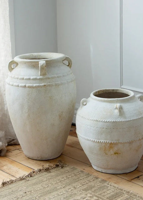 Two large white ceramic pots on a wooden floor with a neutral background