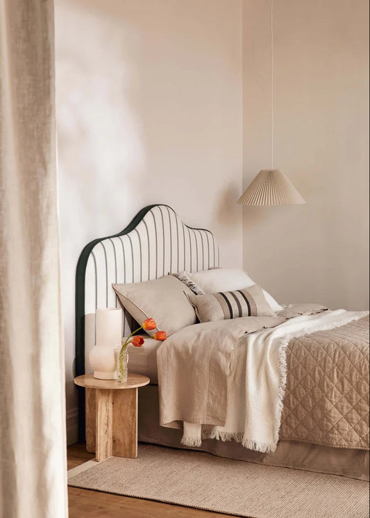 Neatly made bed with beige bedding and pillows in a bedroom setting.