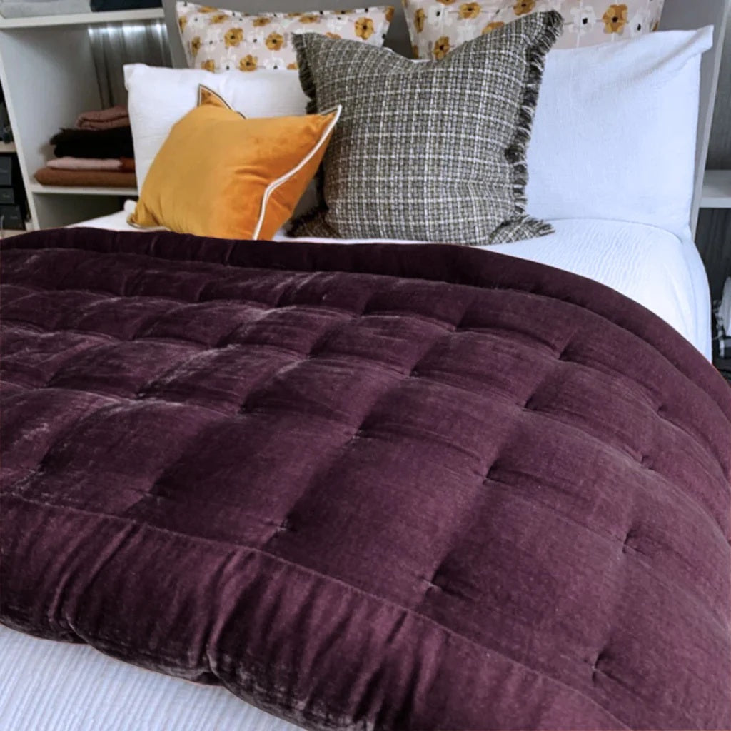 Purple quilted comforter on a bed with patterned pillows