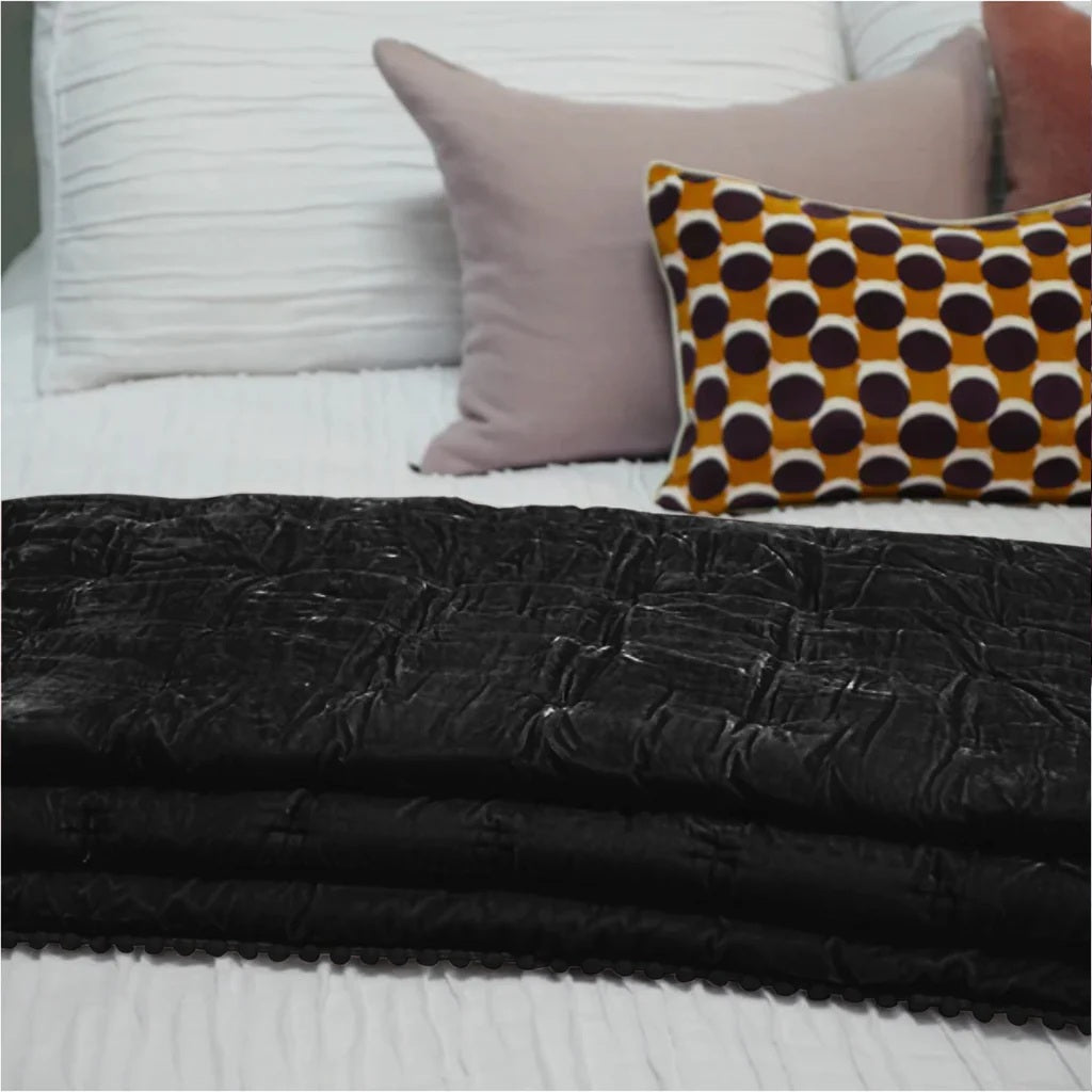 Black textured blanket on a bed with patterned and solid color pillows.