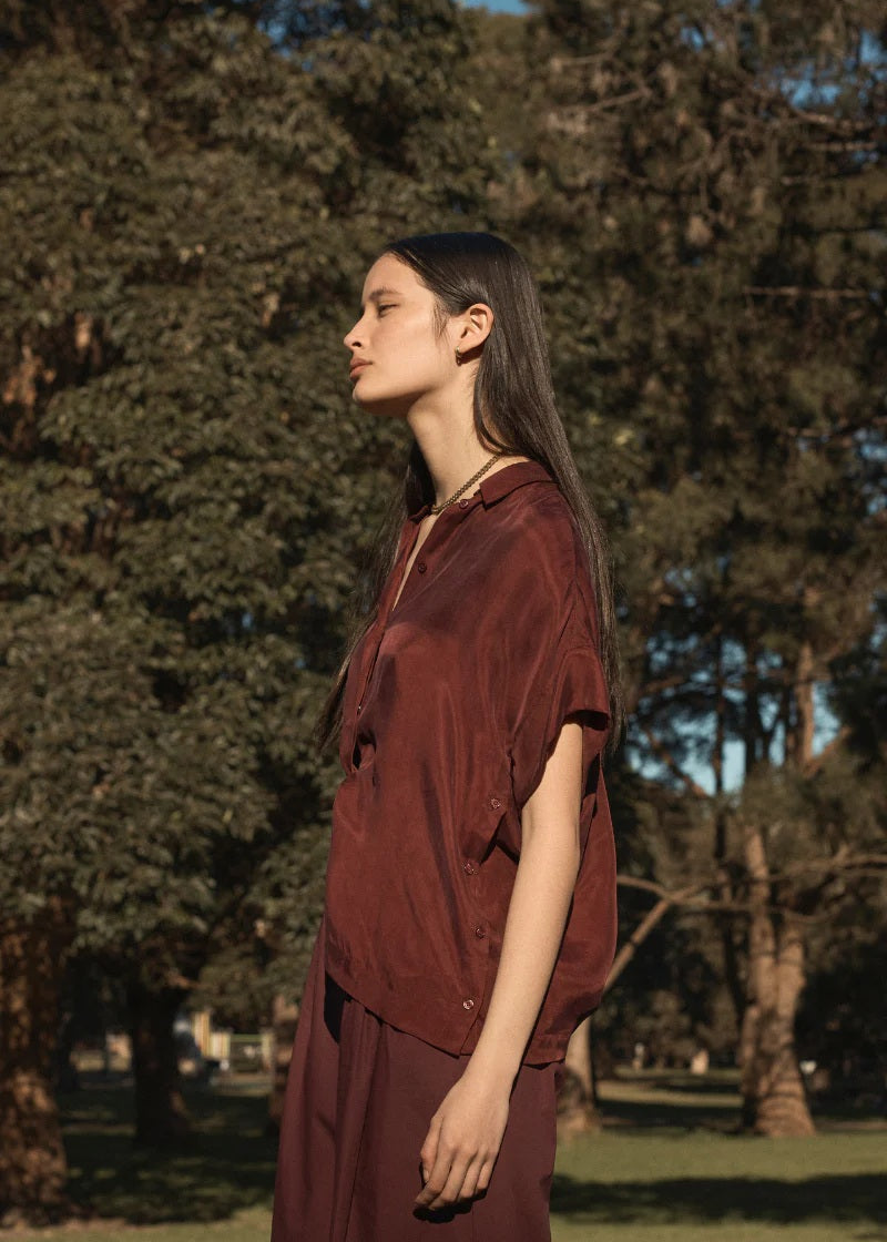 Woman in a burgundy outfit standing in a park with trees in the background