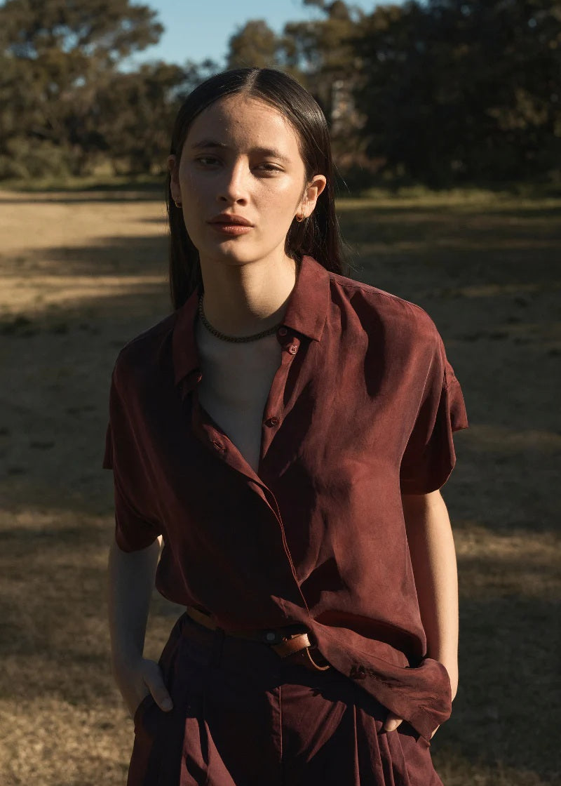 Woman in a maroon outfit standing in a natural setting with trees in the background
