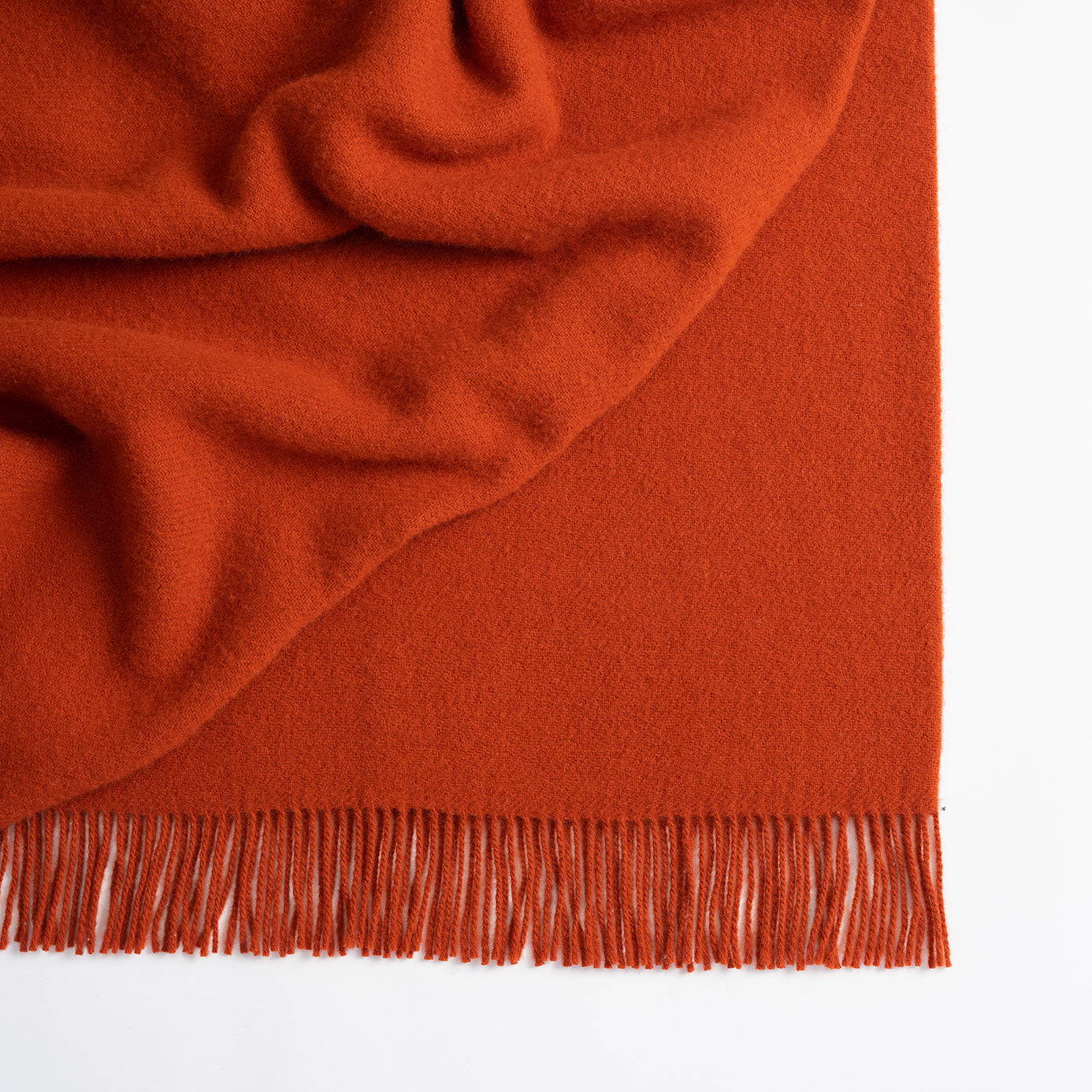 Close-up of a rust-colored blanket with fringed edge on a white background