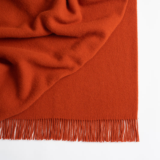 Close-up of a rust-colored blanket with fringed edge on a white background