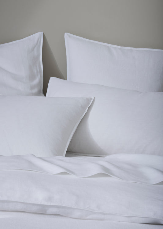 A photo showing a pair of pure white linen pillowcases on a bed, with a sophisticated, top-stitched flanged edge.