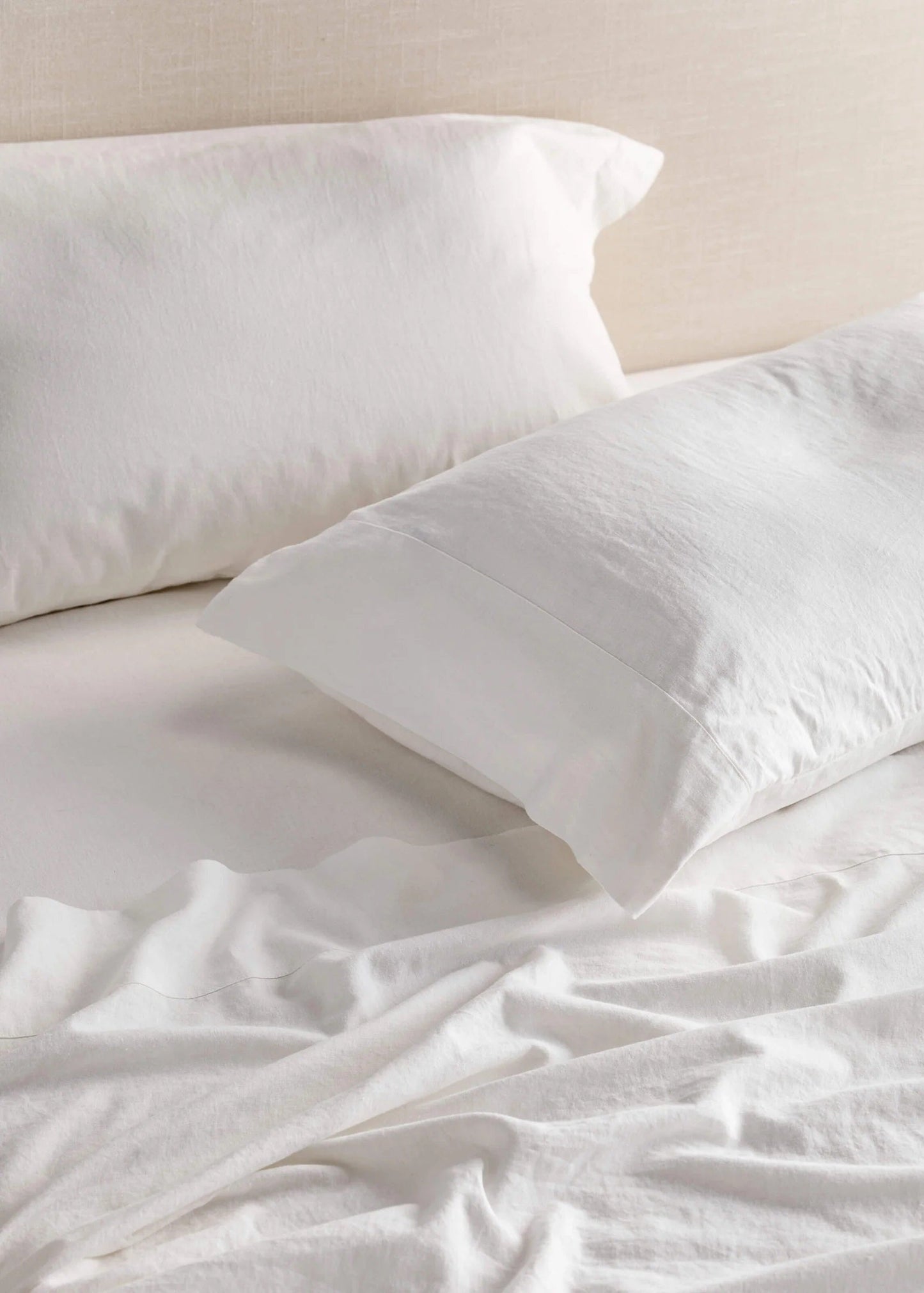 A white flat sheet and two pillowcases on a bed, with the sheet slightly ruffled, giving a luxurious and relaxed appearance.