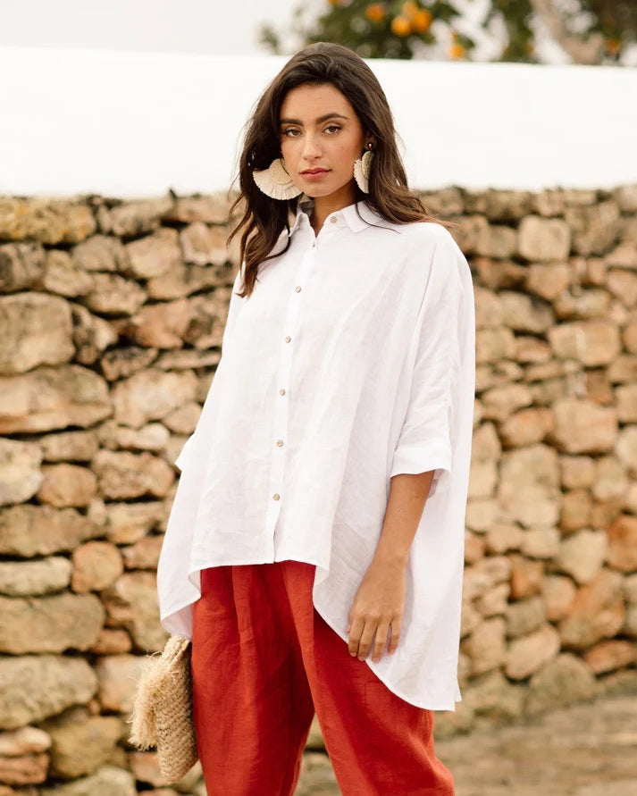 Woman wearing a white shirt and red pants standing in front of a stone wall.