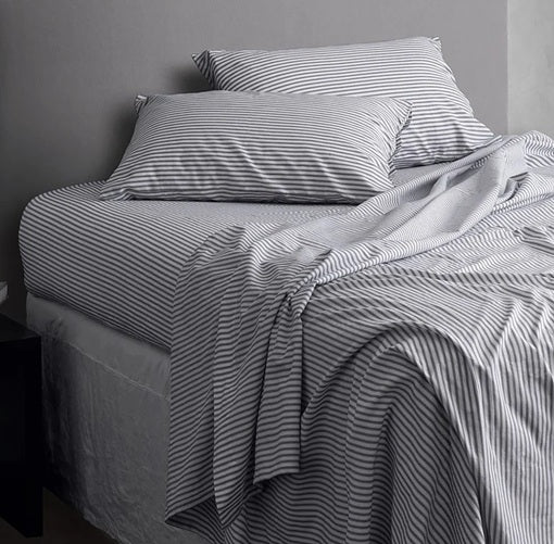 Striped bed sheets and pillows on a bed against a gray wall.