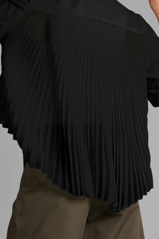 Black pleated blouse worn by a person on a gray background